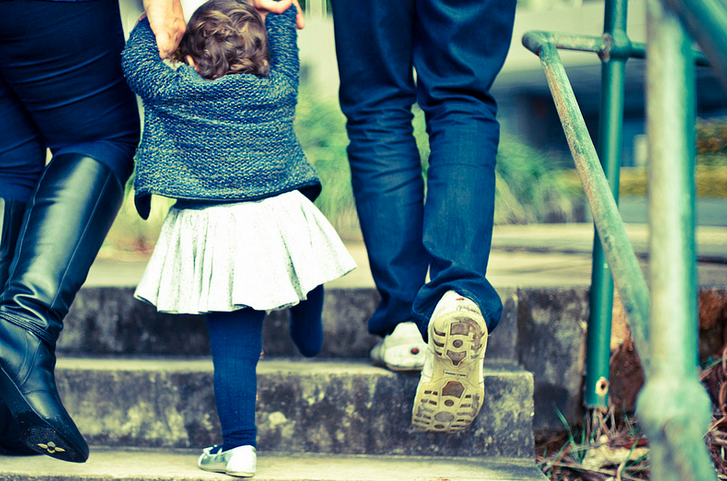 two adults walking up stairs holding child's hands