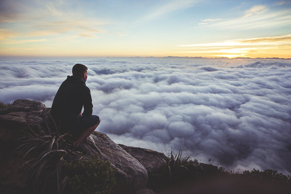the gig economy for talent: hiker sitting at the top of mountain looking out at an expansive sky with clouds