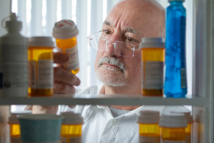 market access: man looking at prescription medication bottles in a medicine cabinet